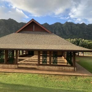 A large wooden house with a green lawn and mountains in the background.