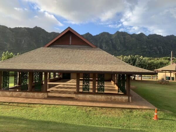 A large wooden house with a green lawn and mountains in the background.